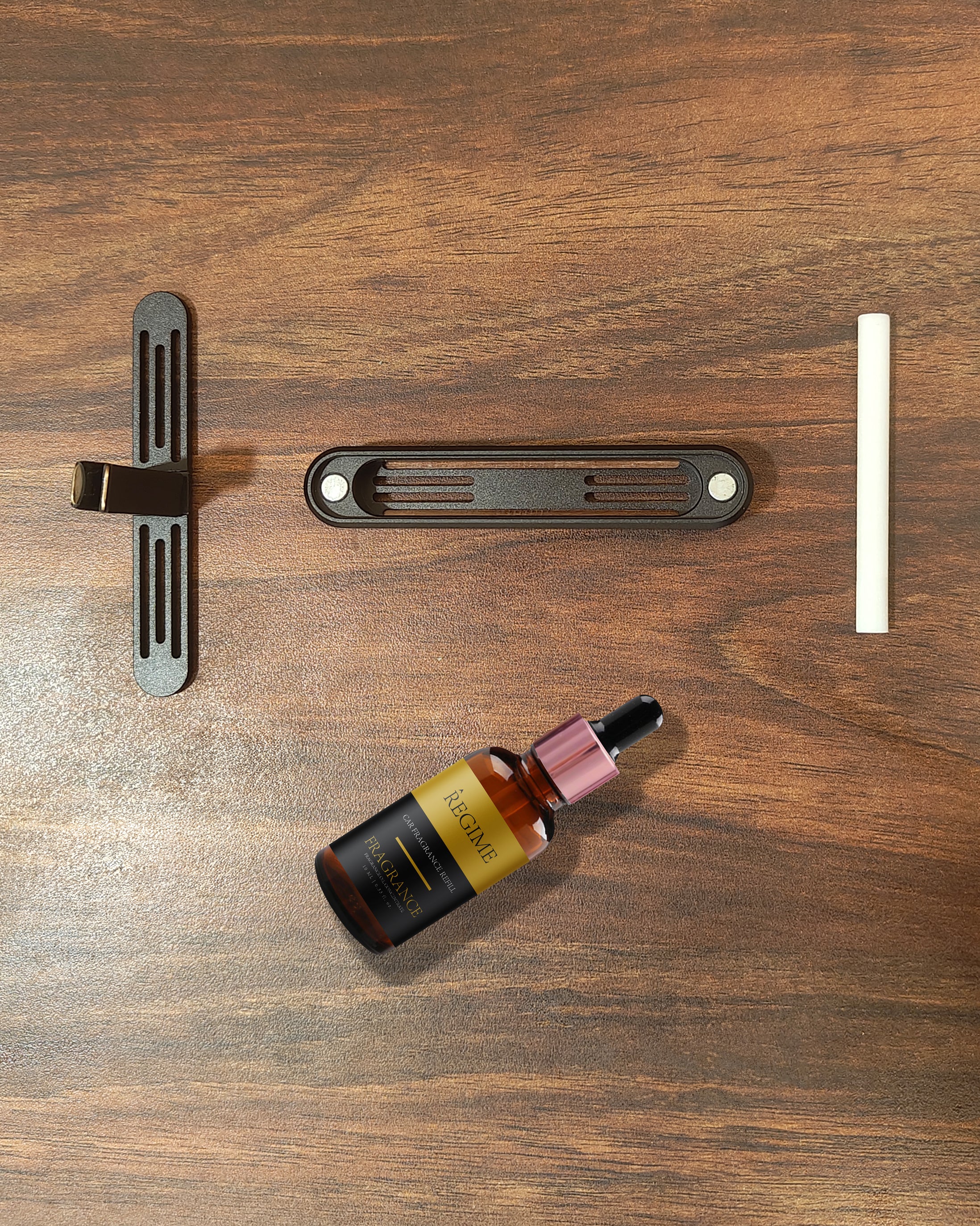 Disassembled Regime Fragrances Charcoal Black car vent clip with wooden front, metal clip, felt tube, and fragrance oil dropper.
